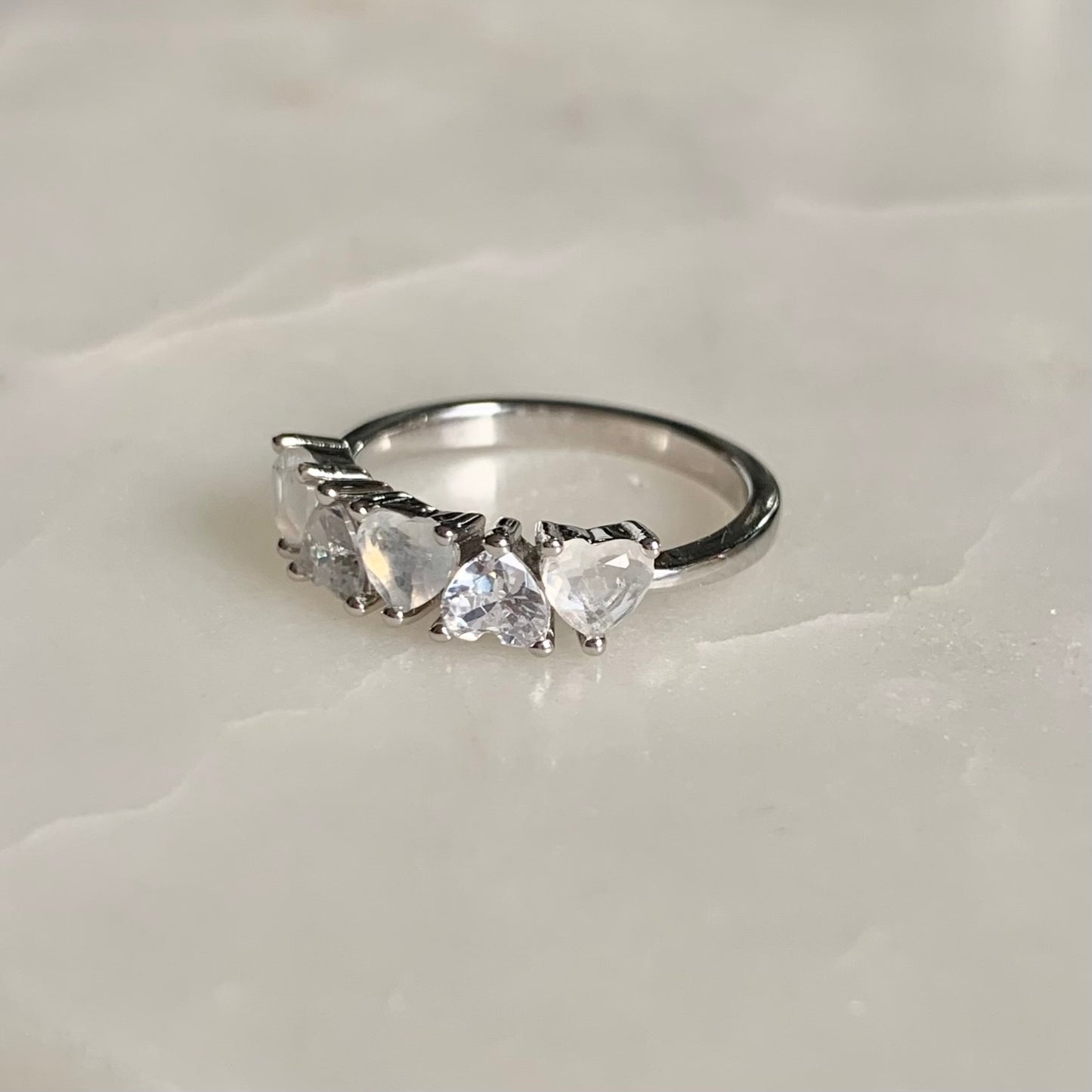 Mila is a stunning five-stone ring with a glistening band. The three heart shaped moonstones and two sparkling cubic zirconia crystals are held in a prong setting and arranged in an alternating pattern.