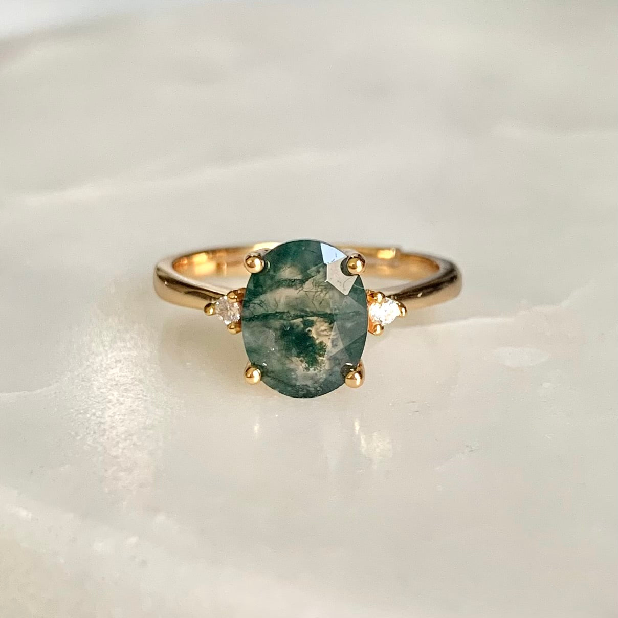 A classic and vintage design gemstone ring. Helena features an oval moss agate stone sits secured in a four prongs setting, embellished with two high quality cubic zirconia crystals accent on each side of the centre gem.