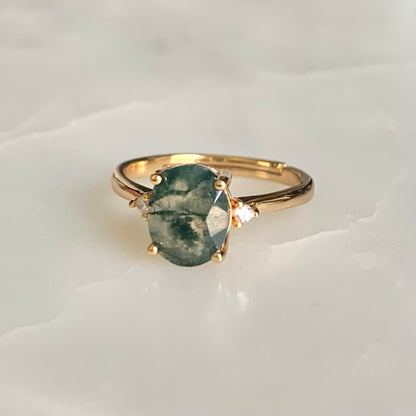 A classic and vintage design gemstone ring. Helena features an oval moss agate stone sits secured in a four prongs setting, embellished with two high quality cubic zirconia crystals accent on each side of the centre gem.