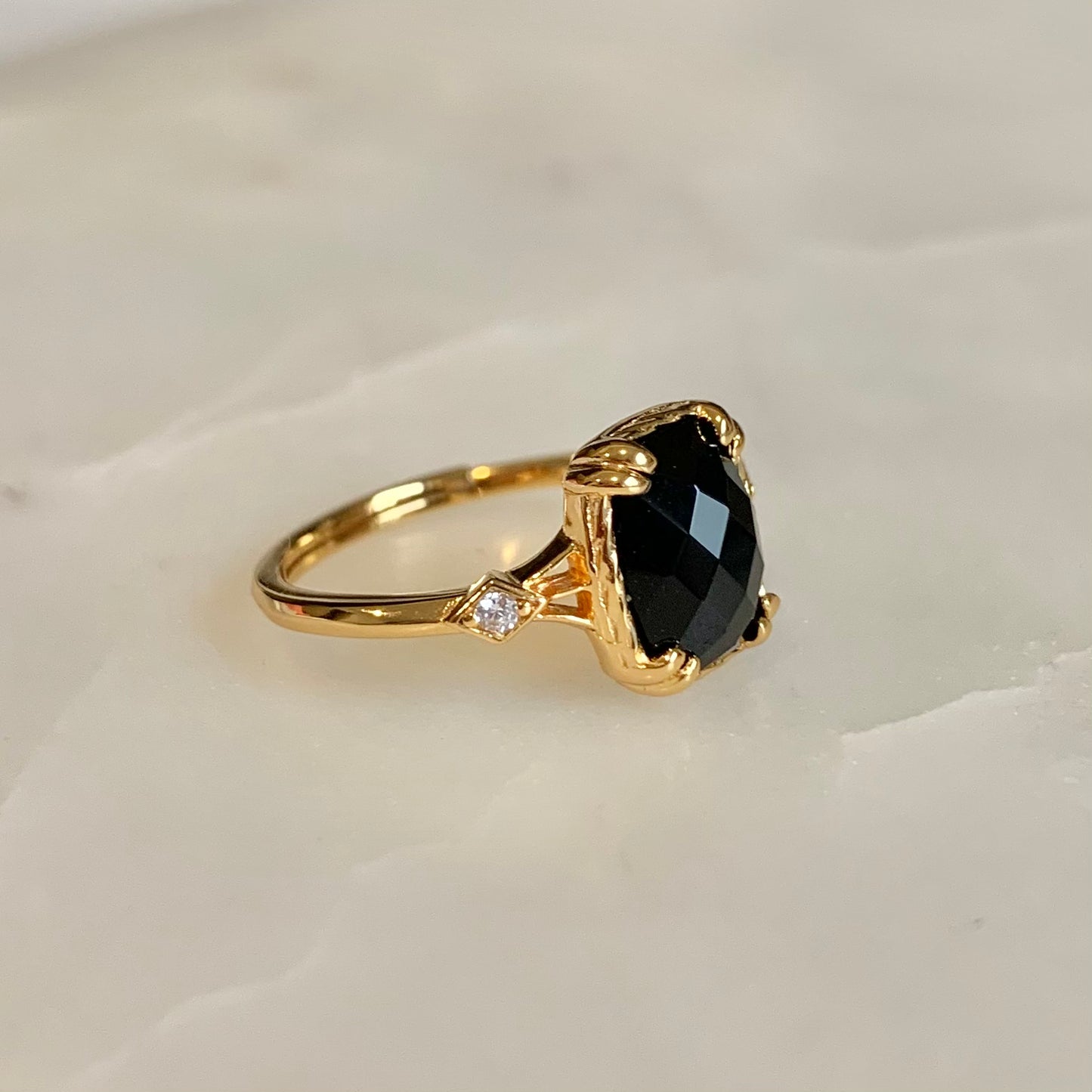 The Jackie Black Agate Ring has a natural black agate set in the centre. This shinny radiant-cut gemstone is held securely by double prongs on its edges, accompanied by two cubic zirconia crystals on both sides.