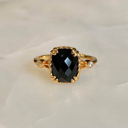 The Jackie Black Agate Ring has a natural black agate set in the centre. This shinny radiant-cut gemstone is held securely by double prongs on its edges, accompanied by two cubic zirconia crystals on both sides.