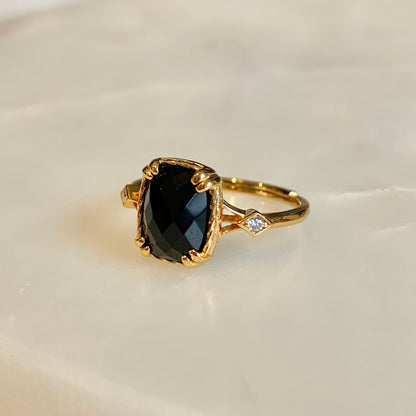 The Jackie Black Agate Ring has a natural black agate set in the centre. This shinny radiant-cut gemstone is held securely by double prongs on its edges, accompanied by two cubic zirconia crystals on both sides.